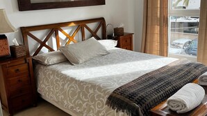 Een keurig opgemaakt bed met een bedsprei met patroon, een houten hoofdbord, een nachtkastje met een lamp en een ingelijst beeld boven het bed.