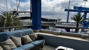 Een balkon met een bank, een tafel en uitzicht op boten en een steiger.