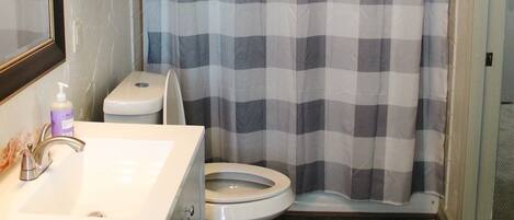 A bathroom with a checkered shower curtain, a toilet, a sink with a mirror, and wooden cabinets.
