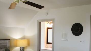 A bedroom with a bed, a ceiling fan, a nightstand, a lamp, a door, and a wall-mounted hat.