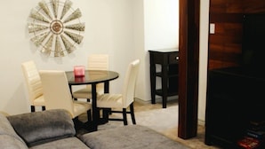 A living area with a grey sofa, a round table with chairs, a decorative wall piece, and a dark wooden cabinet.