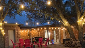 A backyard with a brick building, red chairs, and string lights.