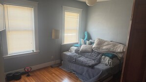 Ein Schlafzimmer mit einem Bett, zwei Fenstern mit Jalousien, einer Stehlampe und einer Tür.