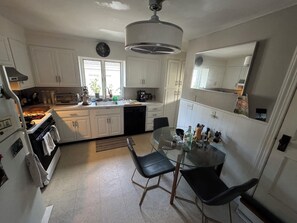 A compact kitchen with white cabinets, a microwave, a sink, and a glass dining table with two chairs. - Welcoming 2-bedroom condo in vibrant Boston neighborhood (Boston)