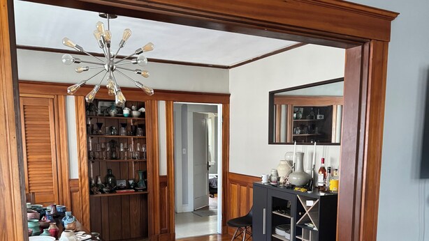 Ein geräumiges Zimmer mit Holzboden, einem Essbereich mit Tisch und Stühlen, einer Küchenzeile mit Schränken und einer Arbeitsplatte sowie einem großen Spiegel an der Wand.