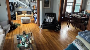 Ein geräumiges Wohnzimmer mit Holzboden, einem schwarzen Ledersessel, einem Glastisch und einem Bücherregal voller Bücher und Dekorationsobjekte.