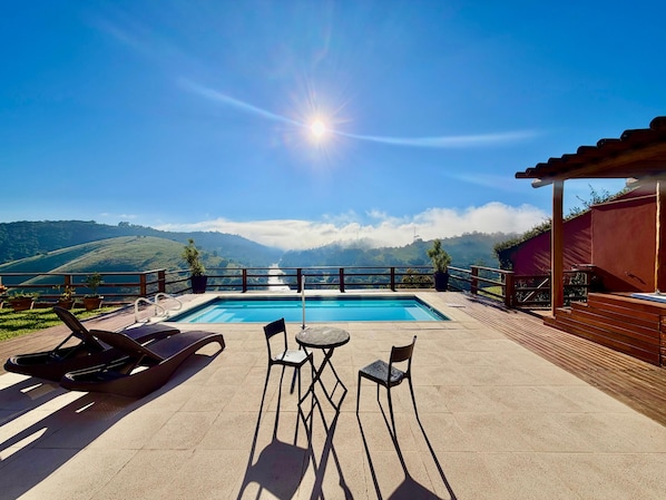 A pool with a view of mountains, outdoor seating, and a pergola.