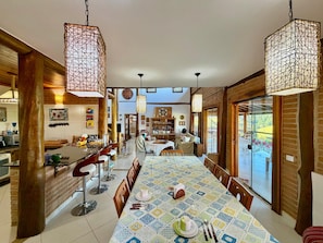 A spacious dining area with a long table, hanging light fixtures, and a view to the outside.