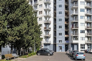 Un edificio residencial de varios pisos con balcones, estacionamiento y un banco.