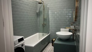 A bathroom with a glass-enclosed shower, a white sink, and a washing machine. - Brand New - 70 m² - Family Friendly - Fast WiFi - 5 min to Old Town (Tbilisi)