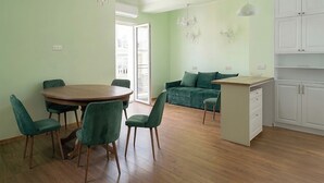 A dining area with a round table and chairs, a sofa, a kitchen with cabinets, and a chandelier. - Brand New - 70 m² - Family Friendly - Fast WiFi - 5 min to Old Town (Tbilisi)
