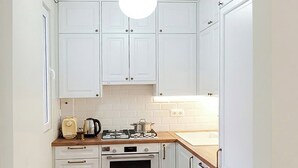 A compact kitchen with white cabinets, a wooden countertop, a stove, and a hanging light fixture. - Brand New - 70 m² - Family Friendly - Fast WiFi - 5 min to Old Town (Tbilisi)