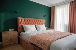 Un dormitorio con cabecera capitonada, mesita de noche de madera, cama con ropa de cama blanca y un amplio ventanal con cortinas.
