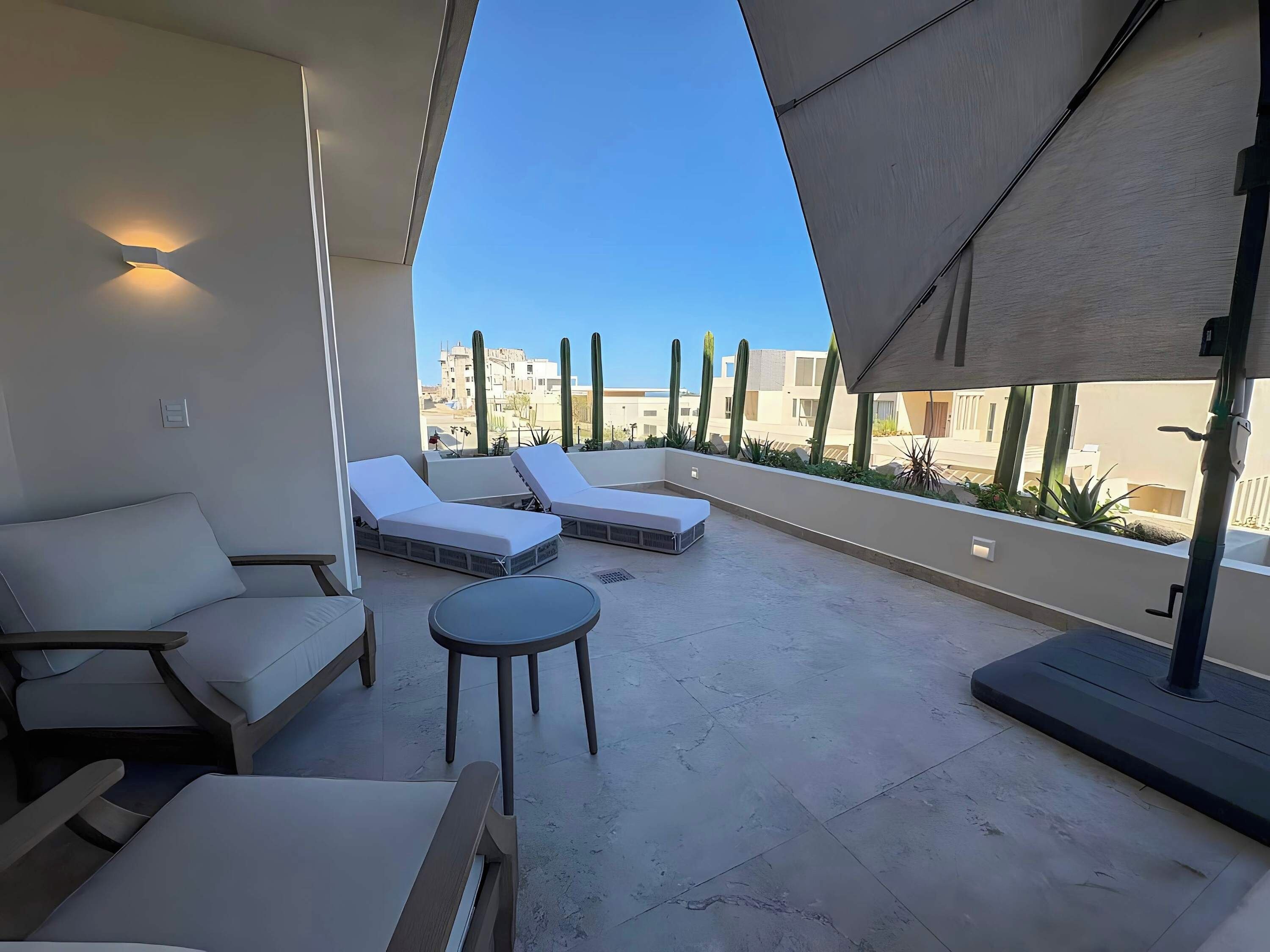 A rooftop terrace with lounge chairs, a small table, and a view of buildings and cacti.