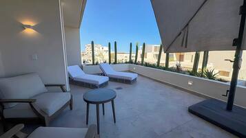 A rooftop terrace with lounge chairs, a small table, and a view of buildings and cacti.