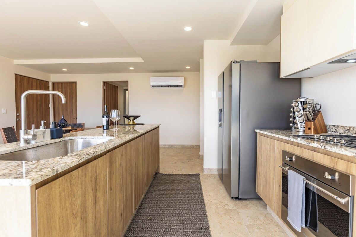 A modern kitchen with a central island, stainless steel appliances, and wooden cabinetry.