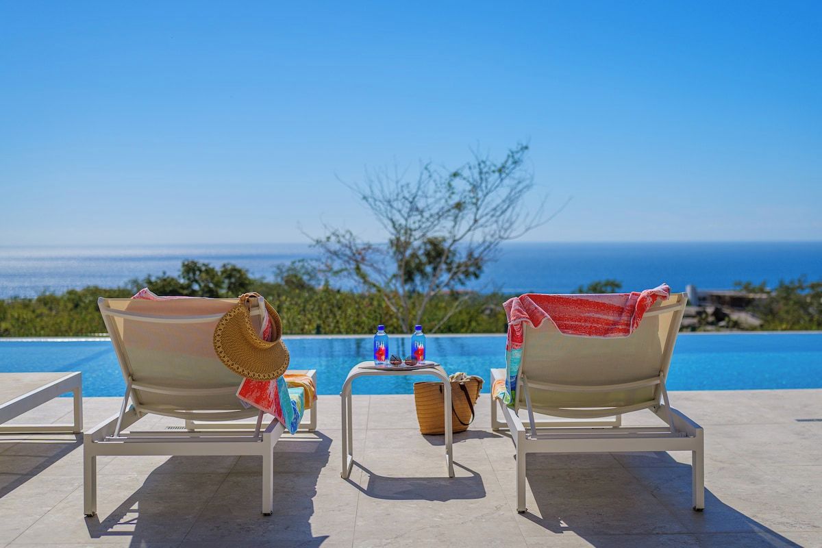 Zwei Liegestühle mit Blick auf einen Pool und das Meer.
