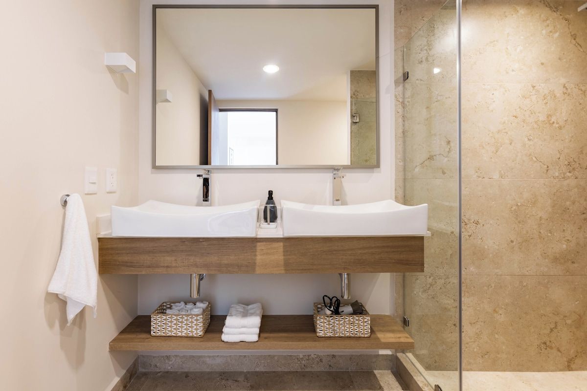 A bathroom with a double sink, a mirror, and a shower area.