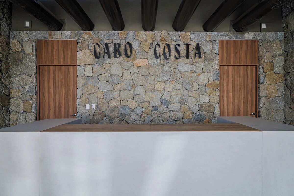 A reception area with a stone wall and wooden doors, labeled 'CABO COSTA'.
