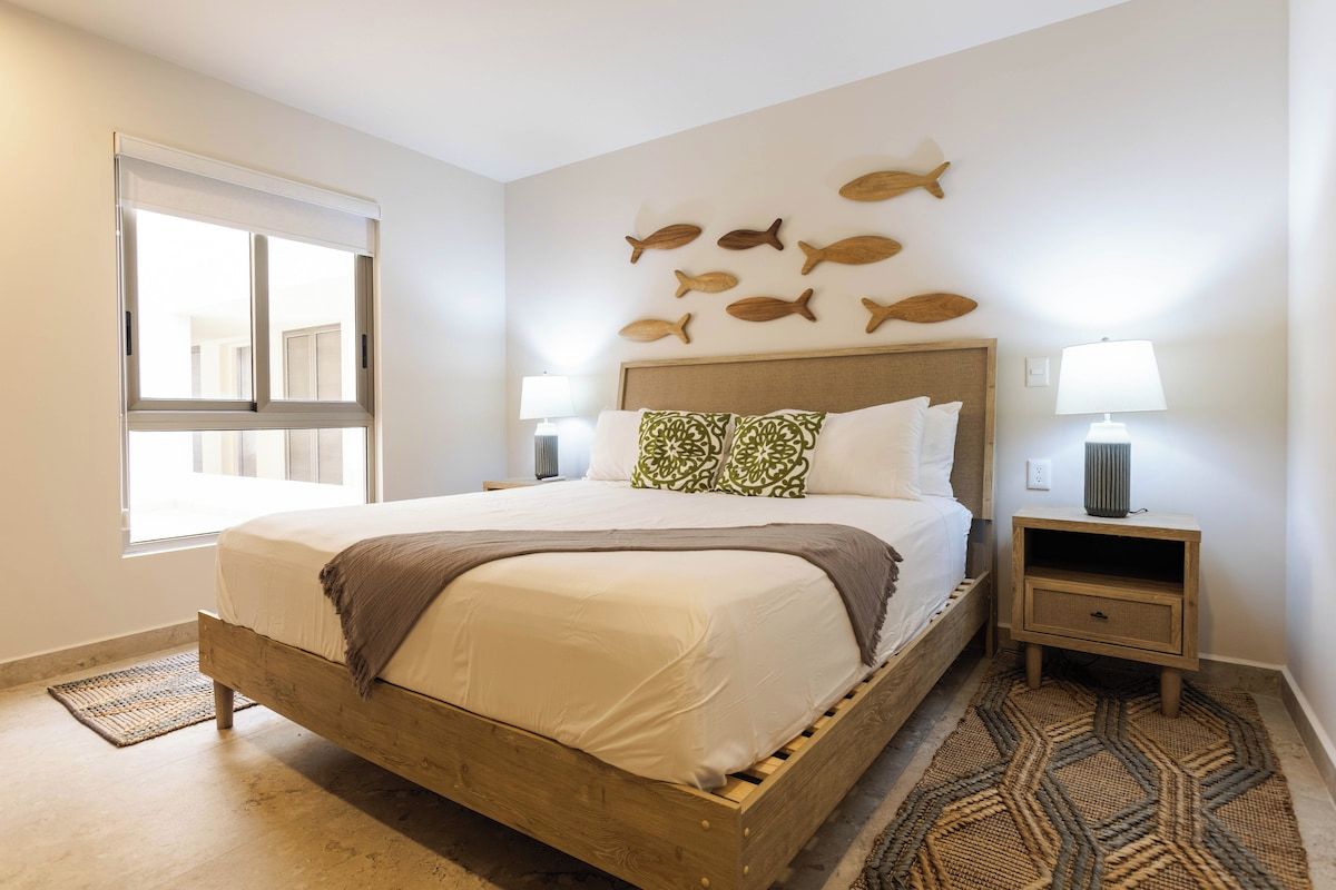 A bedroom with a wooden bed, a wall-mounted fish decoration, a bedside lamp, and a patterned rug.