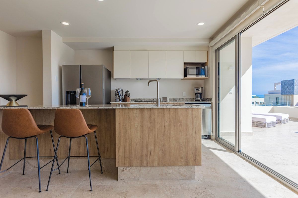 Una cucina moderna con isola in legno, due sgabelli da bar e un'ampia finestra che si affaccia sulla città.