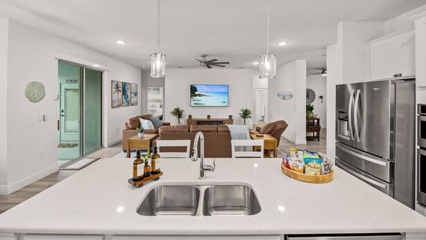 Een moderne keuken met een centraal eiland, roestvrijstalen apparatuur, hanglampen en uitzicht op de woonruimte.