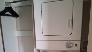 Een kleine wasruimte met een voorlader wasmachine en droger, een klein opbergkastje met lades en een kledingrek.