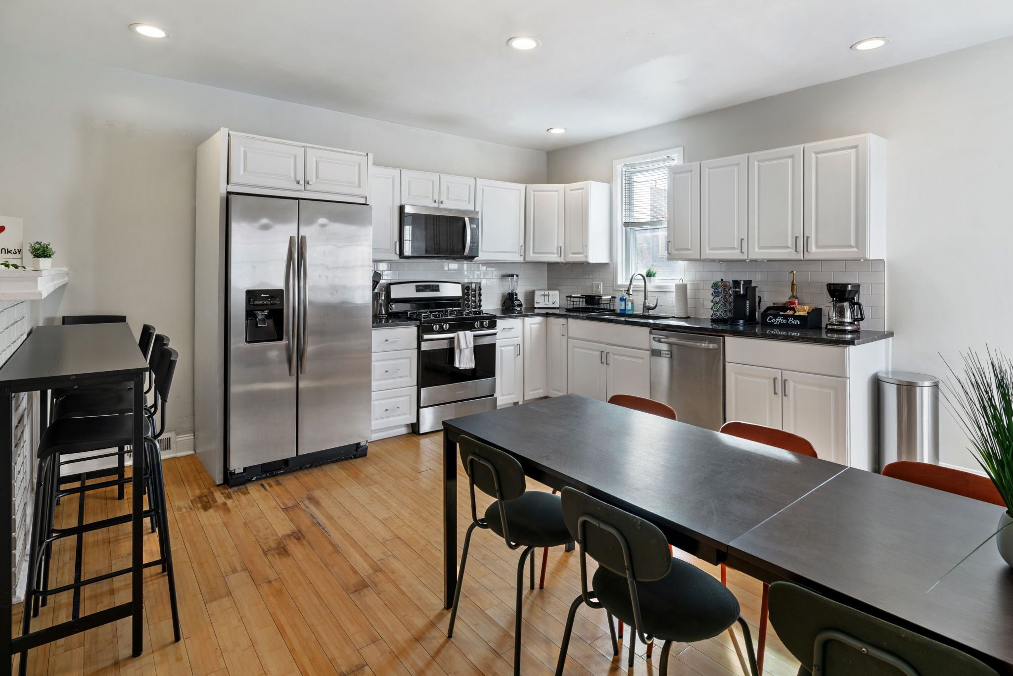 A modern kitchen with stainless steel appliances, white cabinetry, and a wooden floor.