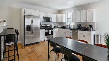 A modern kitchen with stainless steel appliances, white cabinetry, and a wooden floor.