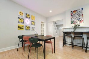 Un comedor con mesa y sillas, una escalera y una pared decorada con caritas sonrientes.