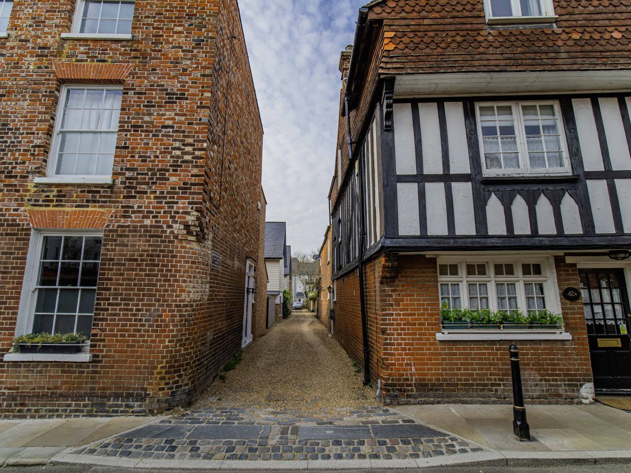A narrow street flanked by traditional brick buildings with white window frames and timber framing.