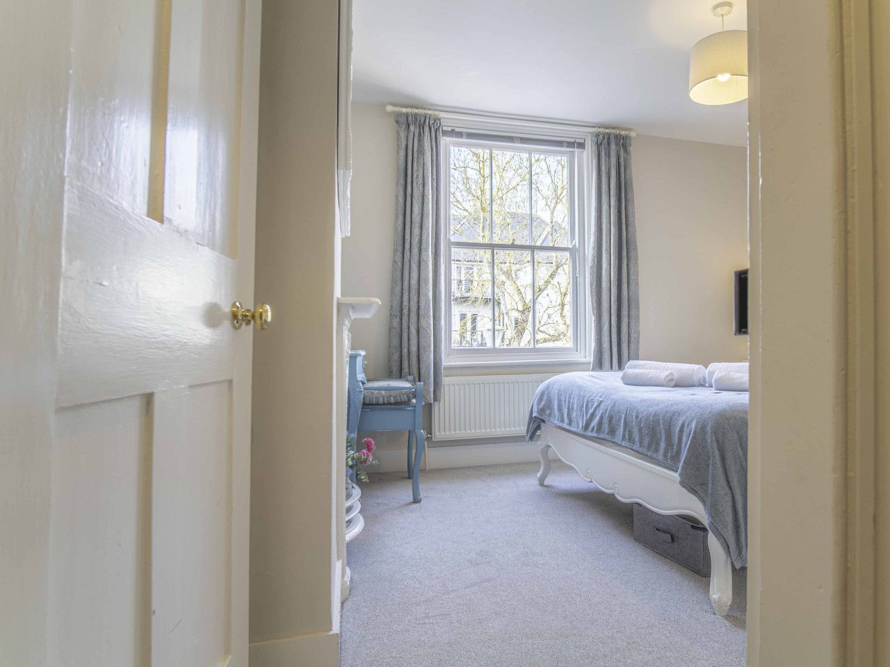 A bedroom with a bed, a chair, a window with curtains, and a radiator.