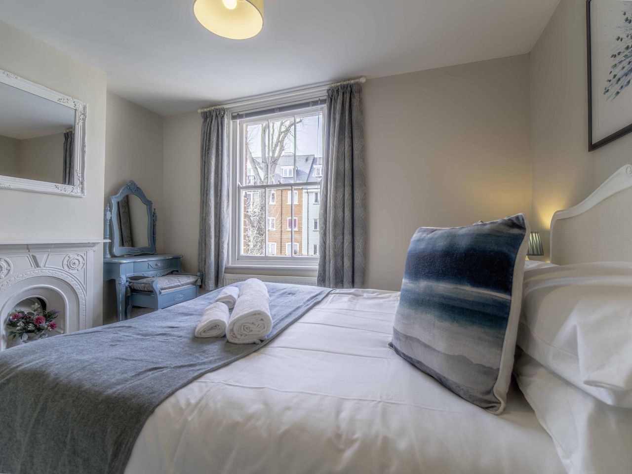 A bedroom with a bed, a dresser, a mirror, and a window with curtains.