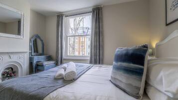 A bedroom with a bed, a dresser, a mirror, and a window with curtains.