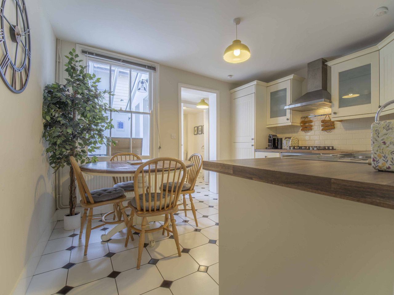 A kitchen with a dining area, featuring a round table with chairs, a potted plant, and a modern pendant light.