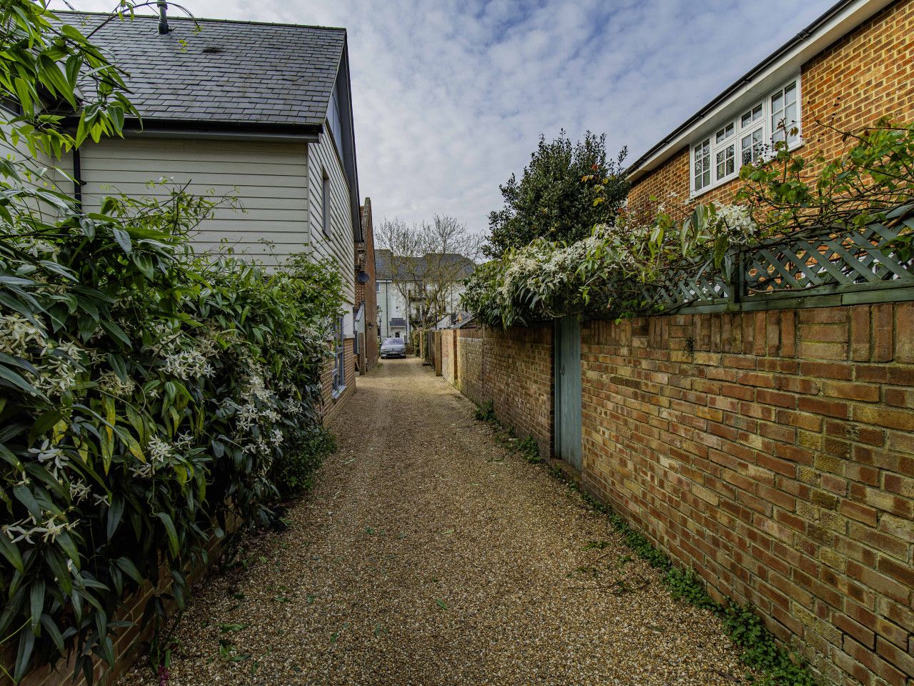 A narrow gravel driveway flanked by brick walls and vegetation.