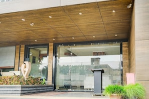 A modern building entrance with a wooden ceiling, glass doors, and a large sculpture. - Super Deluxe Room Hotel Rockland (Kota)
