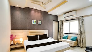 A hotel room with a large bed, a sofa, a nightstand with a lamp, and an air conditioning unit.