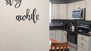 A kitchen with white cabinets, a microwave, stove, and a dining table with chairs. - Modern NewlyFurnished Acadia Apt (Ellsworth)