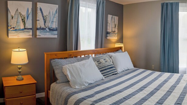 A neatly made bed with striped bedding, a wooden headboard, and two bedside lamps. - Modern NewlyFurnished Acadia Apt (Ellsworth)