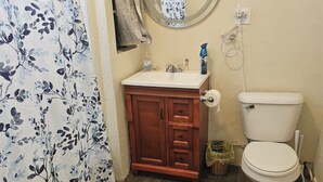 Een badkamer met een houten wastafelmeubel, toilet, spiegel en douchegordijn.