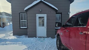 Een tweelaags huis met een witte deur en ramen, een garage en een rode auto ervoor geparkeerd.