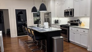 Una cocina moderna con armarios blancos, electrodomésticos de acero inoxidable y una isla central con taburetes de bar.