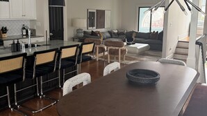 Una cocina moderna con armarios blancos, un comedor con una isla grande, y una sala de estar con sofá y mesa de centro.