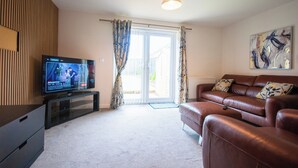 A living room with a television, a sofa, a window with curtains, and a painting on the wall. - Coventry House Near City Centre & Arena (Coventry)