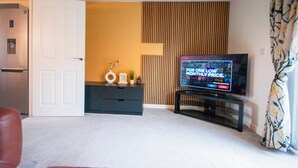 A living room with a television, a door, a small cabinet, and a patterned curtain. - Coventry House Near City Centre & Arena (Coventry)