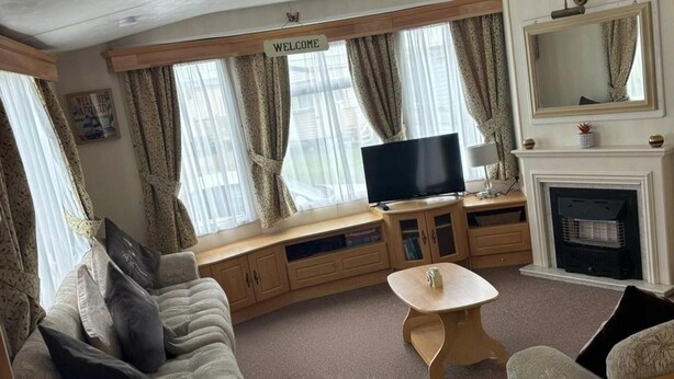 A cozy living room with a sofa, a television, a fireplace, and a 'WELCOME' sign above the windows. - 14 South Happy Days - Sleeps 6 Pet Free Caravan (Skegness)