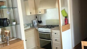 A compact kitchen with a gas stove, oven, and a small countertop area. - 14 South Happy Days - Sleeps 6 Pet Free Caravan (Skegness)