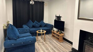 Una sala de estar con un sofá azul, una mesita de madera, un televisor de pantalla plana y una chimenea.