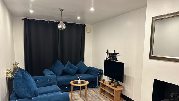 Una sala de estar con un sofá azul, una pequeña mesa redonda, un televisor de pantalla plana, una chimenea y una lámpara en el techo.
